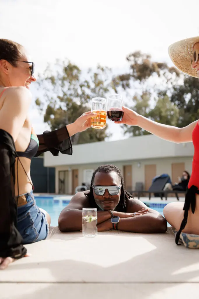 Govino Shatterproof Beer Can Glass in front of a man in a pool with two women sitting in front of him cheersing their Govino Shatterproof Wine Glasses